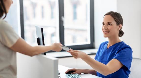 Patientin gibt Krankenshwester Krankenkassenkarte
