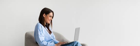Frau mit Laptop sitzt auf Sessel